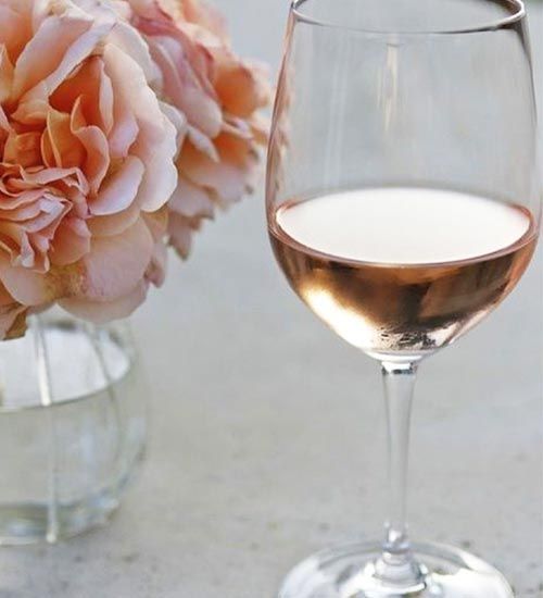 A glass of rosé wine and a vase of peach-colored flowers.