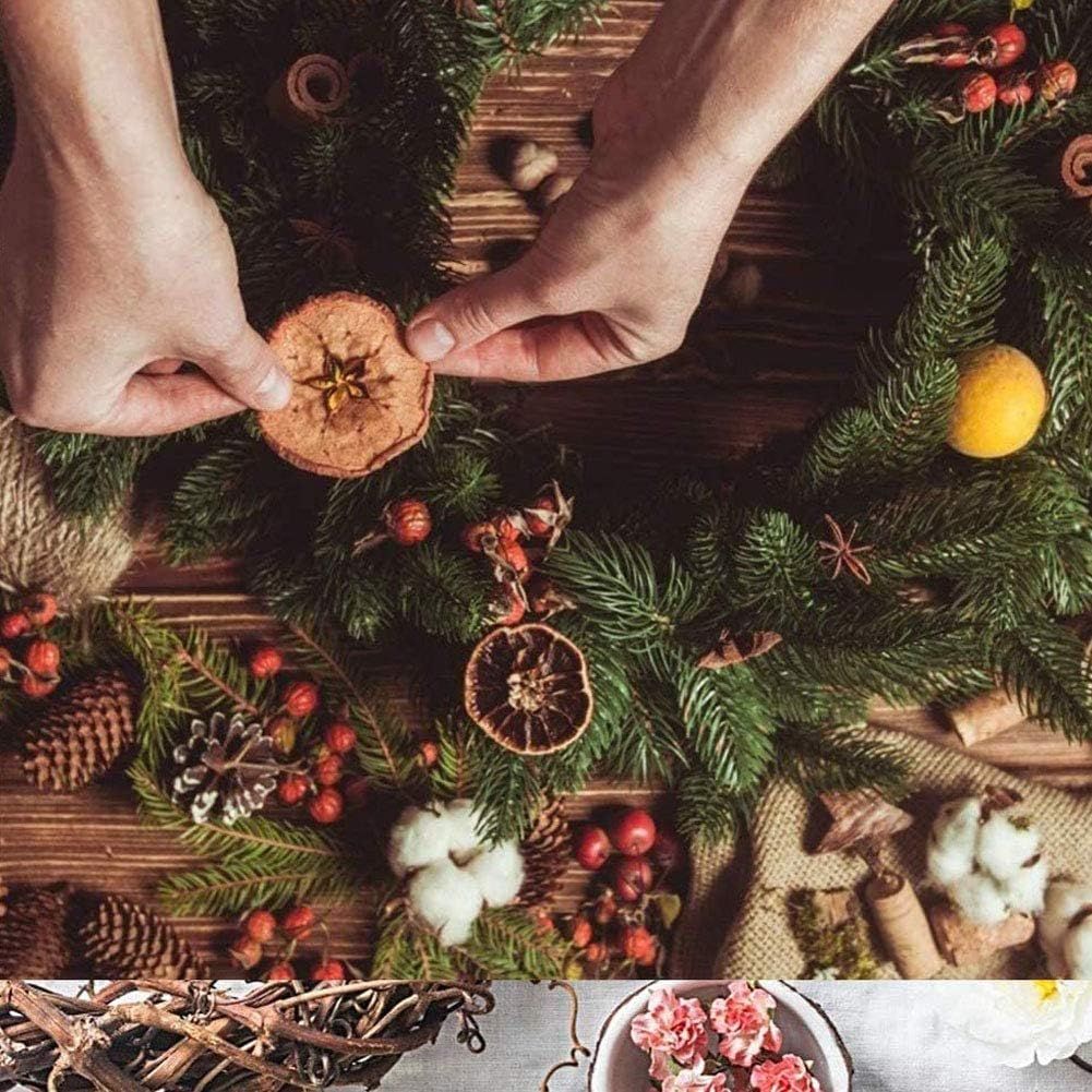 Hands decorating a Christmas wreath with dried fruit and greenery on a wooden table.