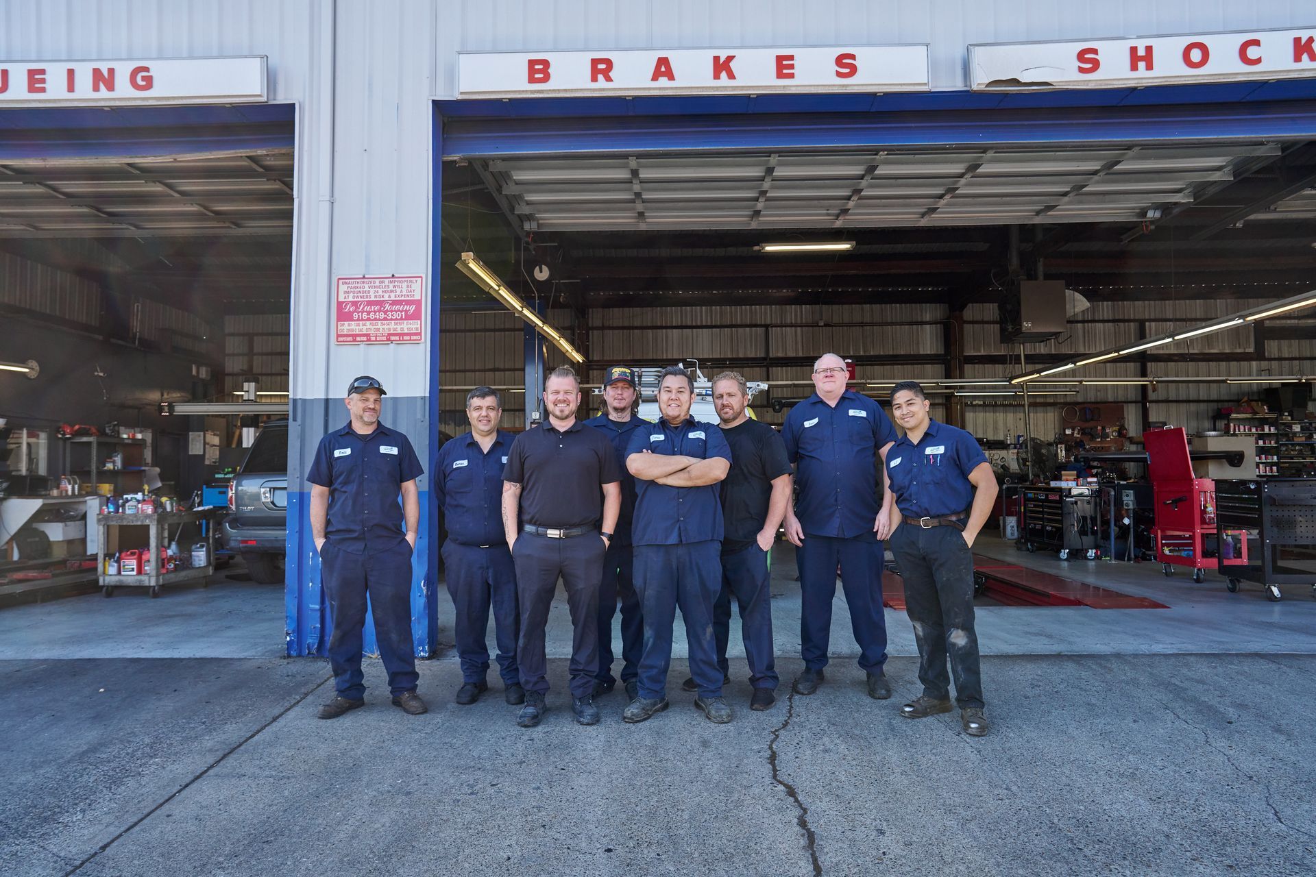 Auto Repair Team Standing Outside Garage With Cars On Lifts | Linville Brothers
