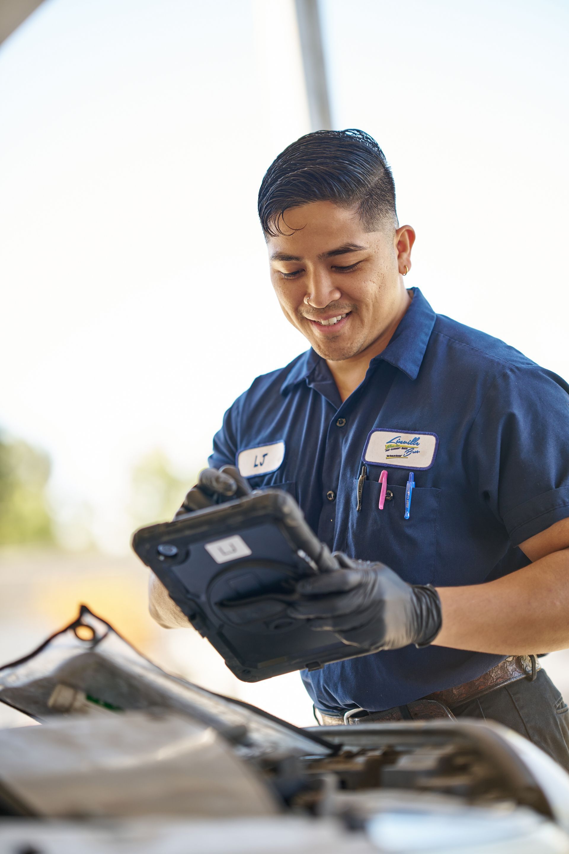 Auto mechanic using a tablet to diagnose a car, smiling | Linville Brothers