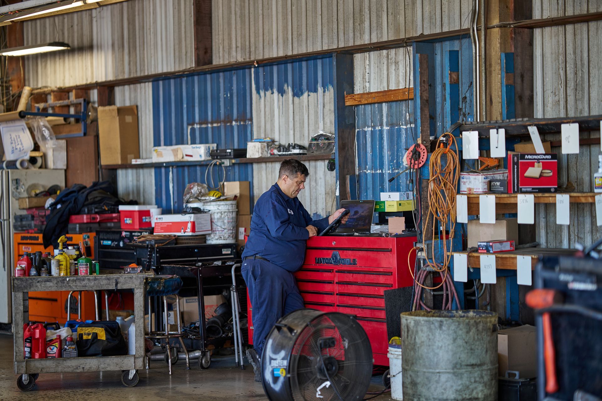 Mechanic using a tablet in a cluttered auto repair shop, standing near a red toolbox | Linville Brothers