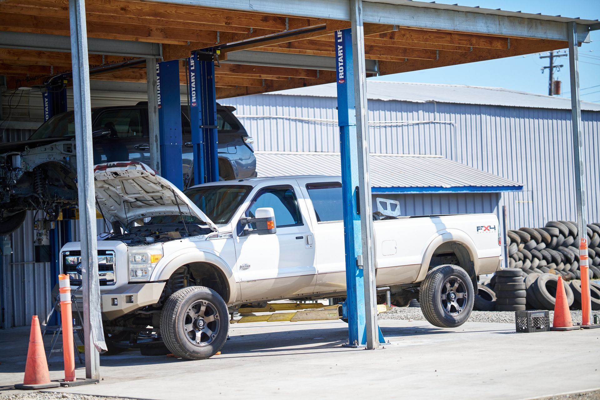 White truck with hood open in auto repair shop, another truck lifted above | Linville Brothers