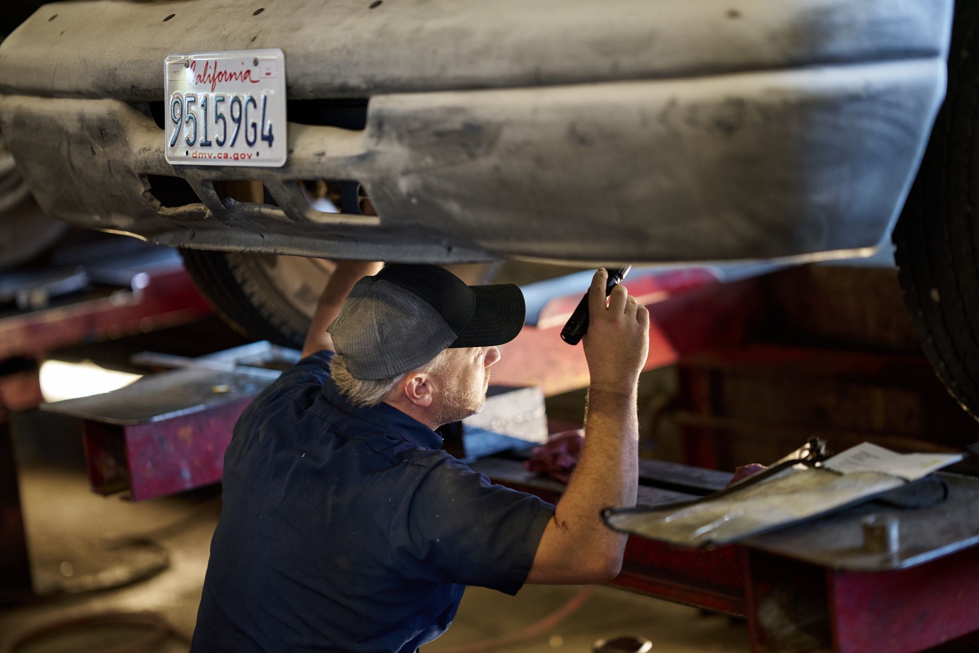 Mechanic working under a car, holding a flashlight | Linville Brothers