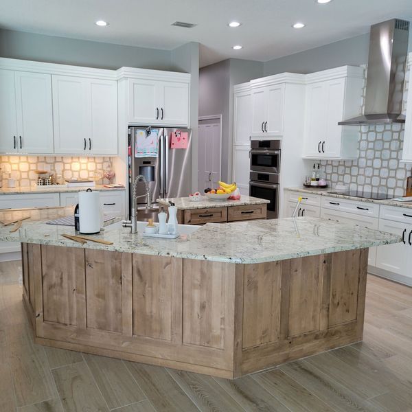 A modern kitchen features white cabinetry, a large natural wood-tone island with a granite countertop, and gray walls.