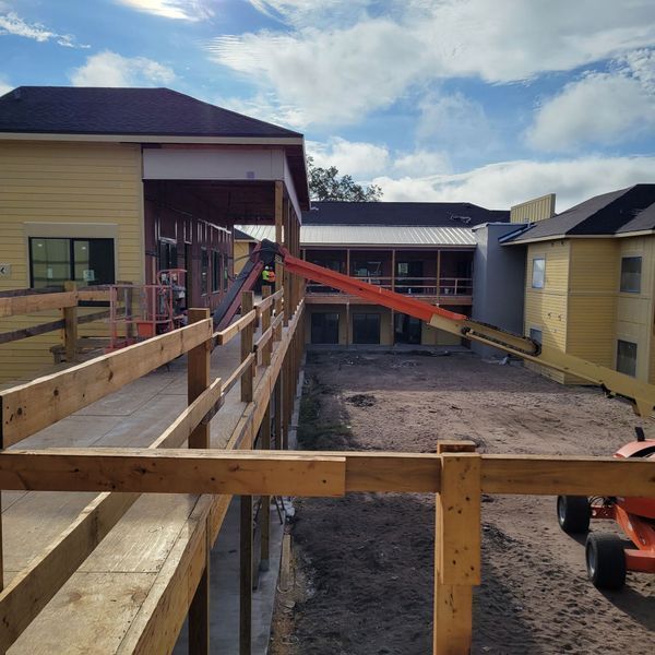 Construction site: wooden ramp, yellow building, orange lift, blue sky.