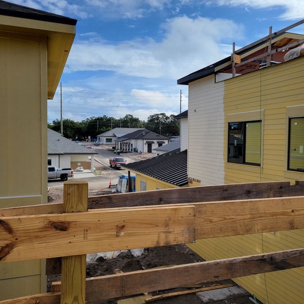 Construction site with buildings; yellow and white siding, wooden beams, blue sky.
