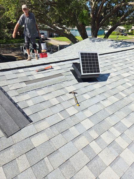 Man on a roof repairs shingles; a solar panel sits nearby.