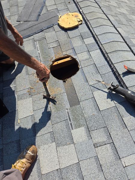 Man using a hammer to work on a hole in an asphalt shingle roof.