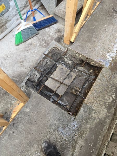 Square hole in concrete floor with exposed rebar and small central block. Construction setting.