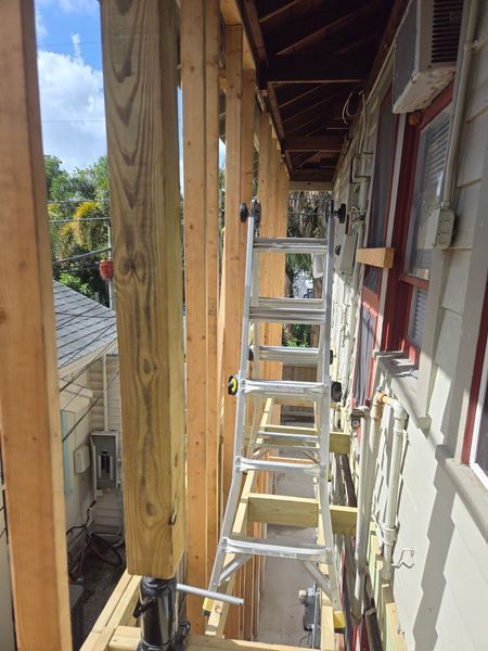 Construction site: ladder inside new wooden frame, attached to a building, partially blocking a walkway.