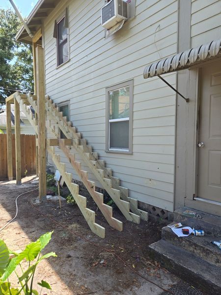 Wooden staircase built on side of a light-colored two-story building.