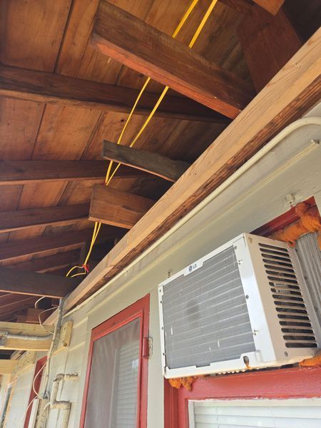 Yellow electrical wires run across a wooden ceiling. An AC unit is mounted below.