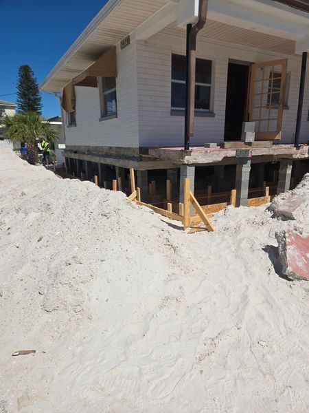 House under construction raised on wooden supports, with sand around it.