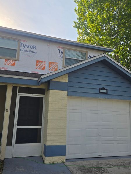 Blue and yellow house exterior under construction, with Tyvek wrap and garage.