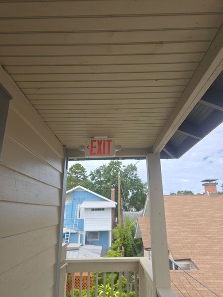 Exit sign above a balcony opening to a residential neighborhood, light blue house visible.