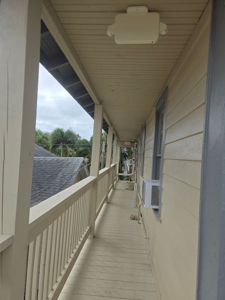 Wooden porch with railing and a roof extending down a building's side, overcast sky.