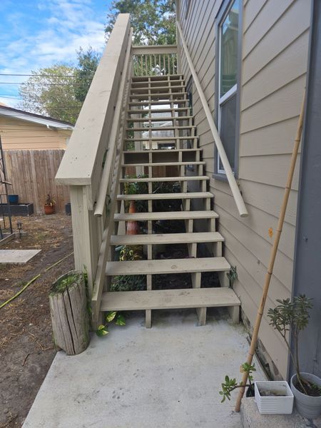 Wooden outdoor staircase against a house, leading upward. Concrete landing below.