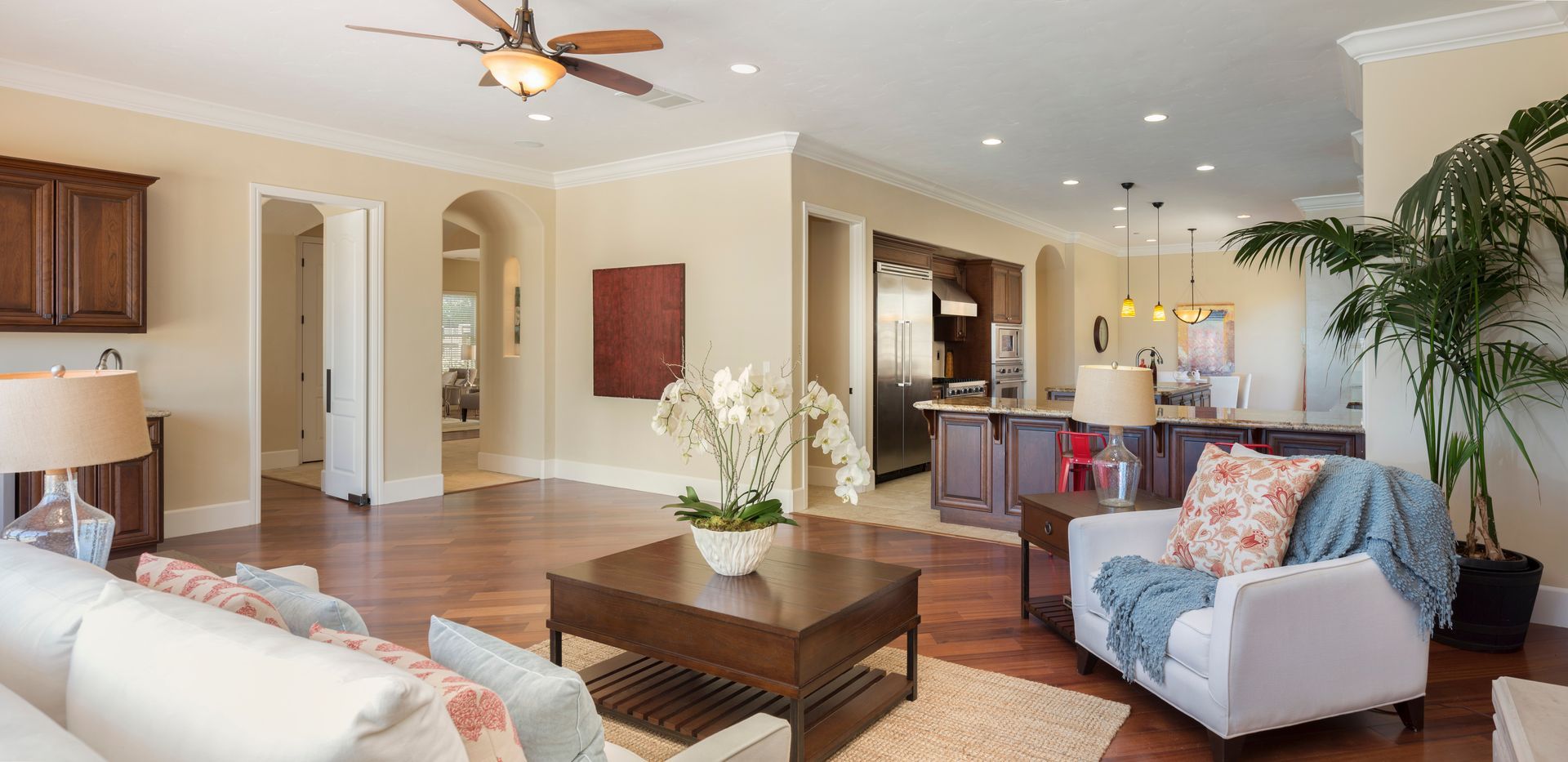 Living room interior with hardwood floors, white furniture, and a kitchen in the background.