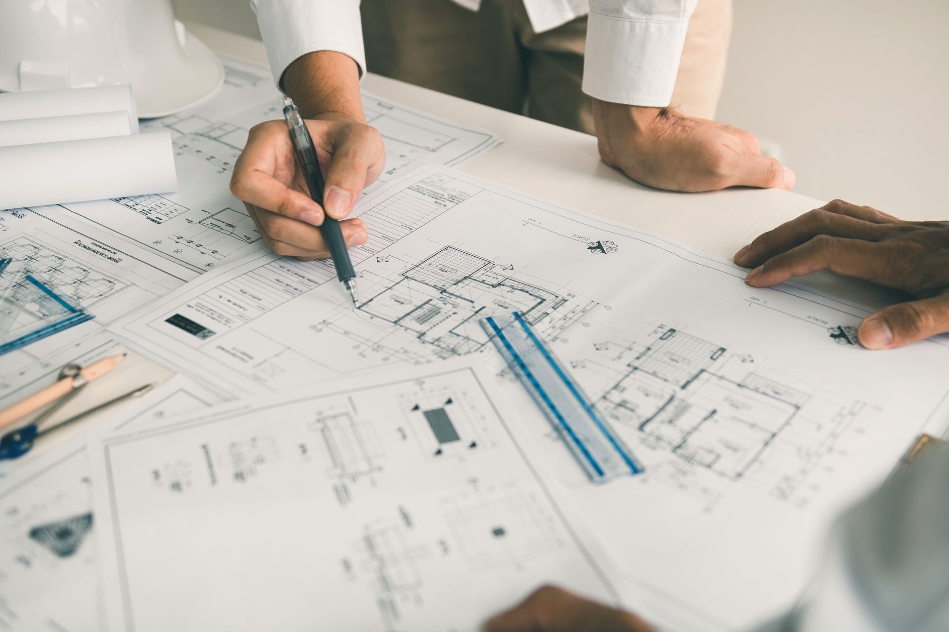 Architects reviewing blueprints with pen and ruler on a white table.