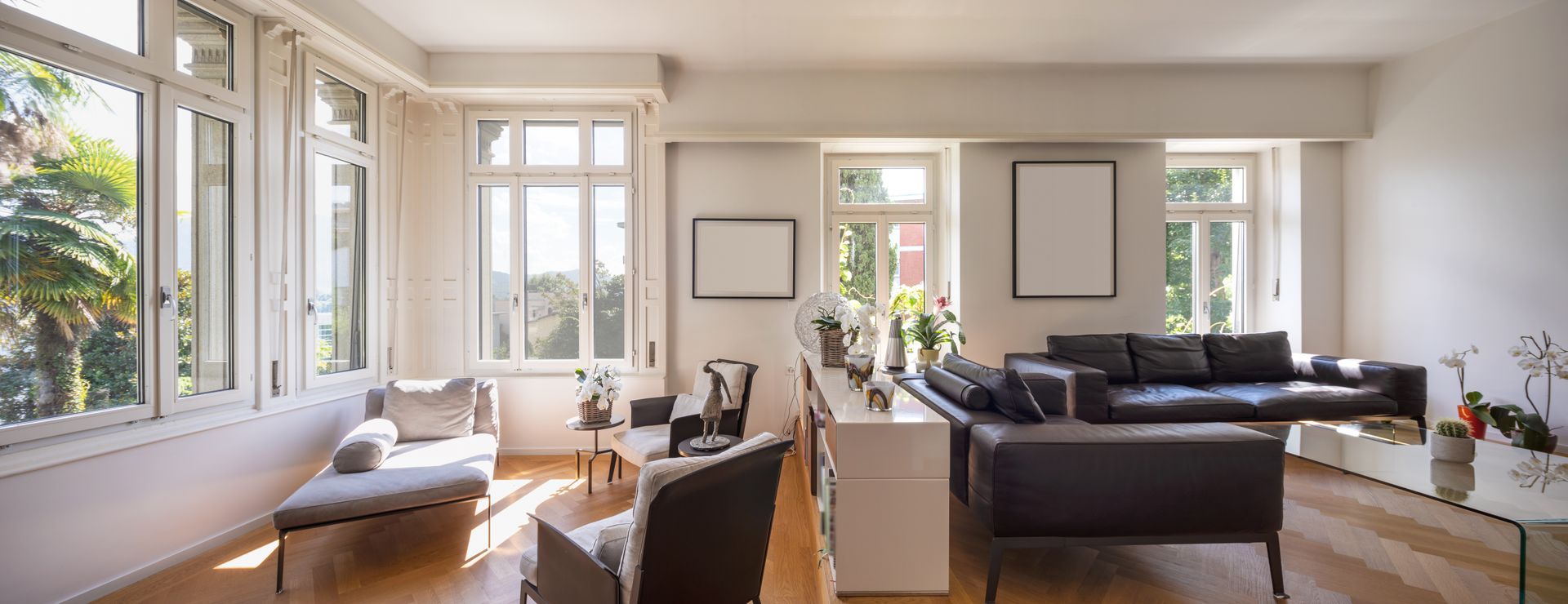 Bright living room with large windows, wooden floor, and a dark leather sofa.