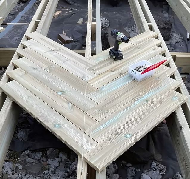 Herringbone pattern decking being installed on wooden supports with a drill and screws nearby.