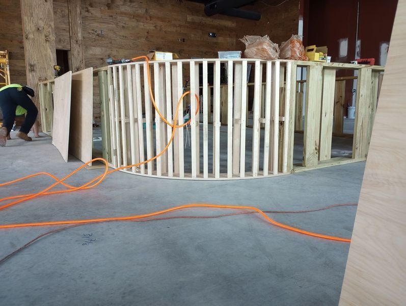 Construction of a curved bar frame with wooden studs and concrete floor.