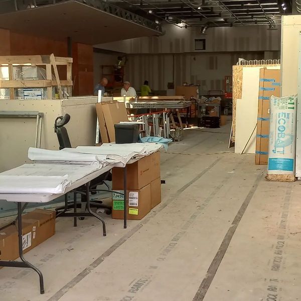 A construction site interior featuring a temporary work table with blueprints, cardboard boxes, and building materials.