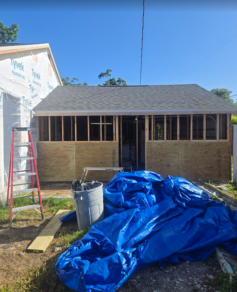 Construction of a small building. Walls are framed with insulation exposed. A blue tarp and ladder are present.
