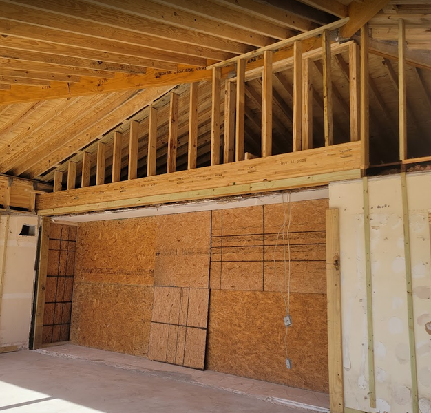 Interior of a building under construction, showing wooden framework, OSB panels, and exposed rafters.