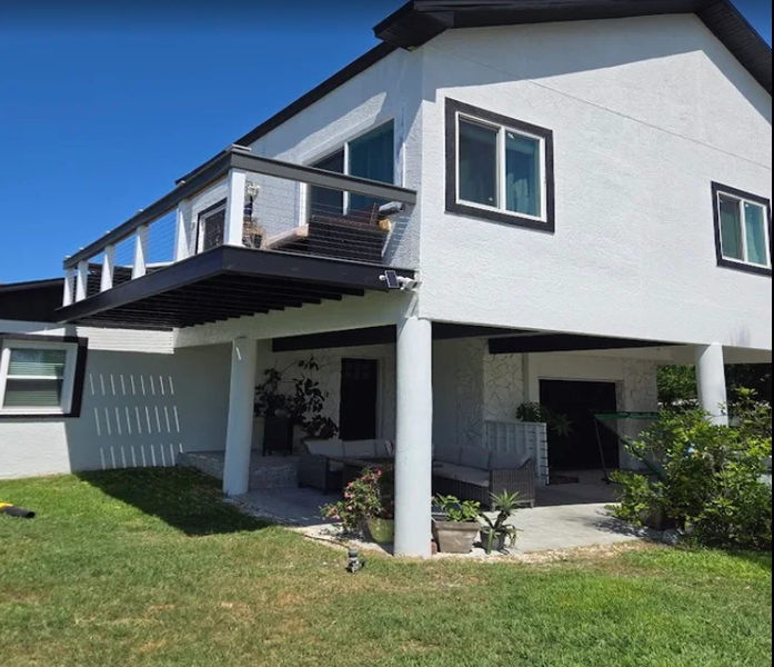 Two-story white house with black trim, balcony, and covered patio area, under blue sky.