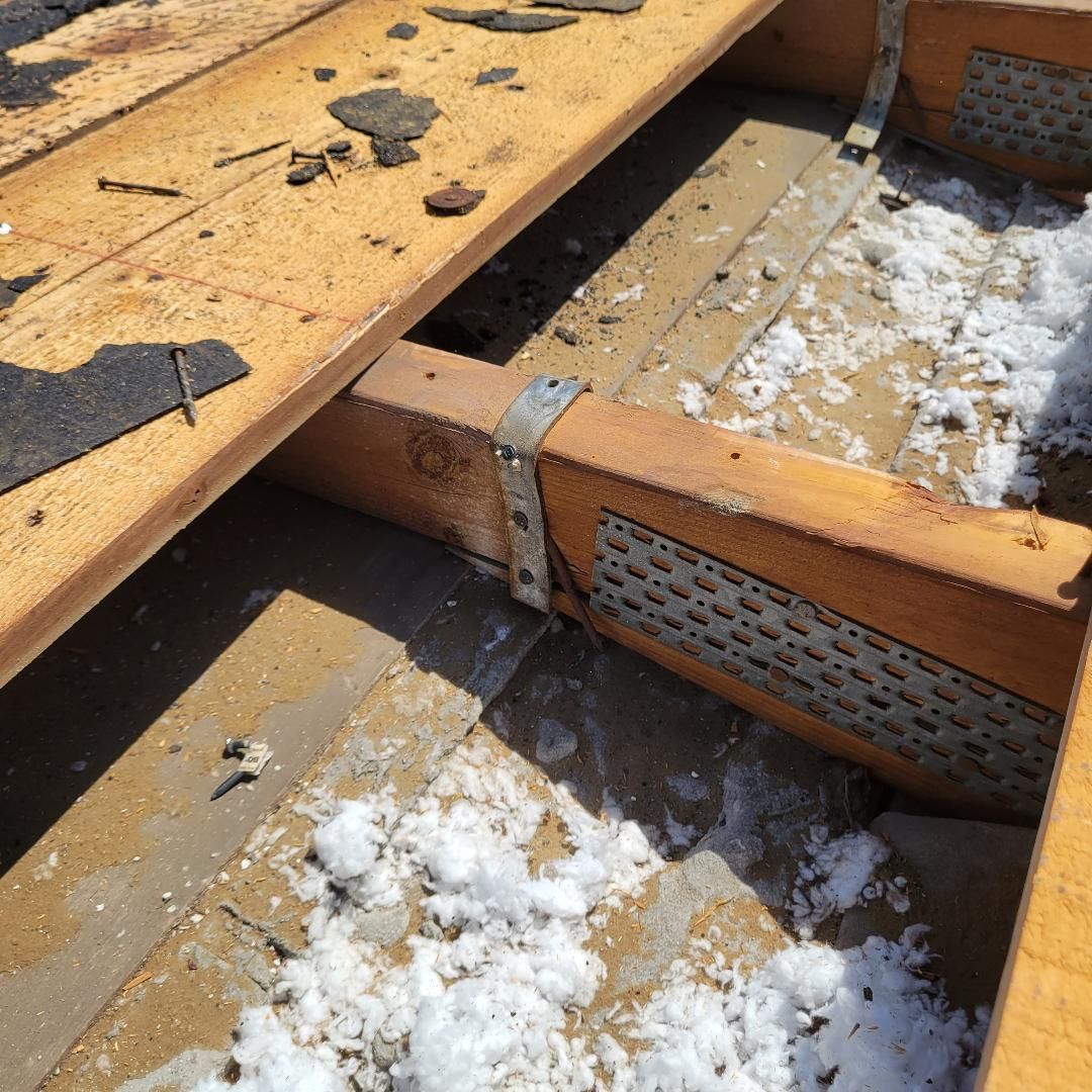 Roofer in work boots installing dark gray roof tiles on a sunny day.