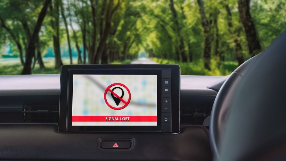 Dashboard GPS with a blocked location icon, set against a blurred road through trees.