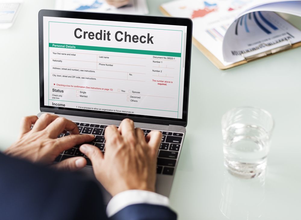 Person typing on laptop showing a credit check form on a white desk with water glass.