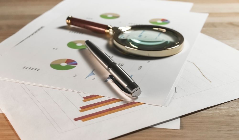 Magnifying glass and pen on printed charts with graphs, indicating analysis.