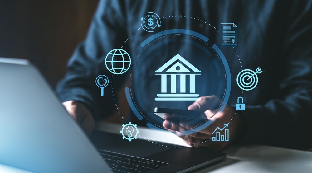 Person using a laptop and phone, with digital bank icon and financial symbols overlay.