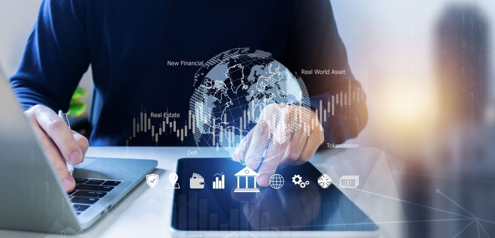 Person working on a laptop and tablet with digital financial data and a world map overlay.