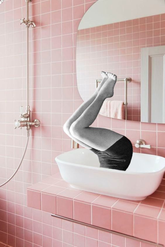 Person's legs sticking out from a sink in a pink tiled bathroom. Black shorts and bare feet visible.