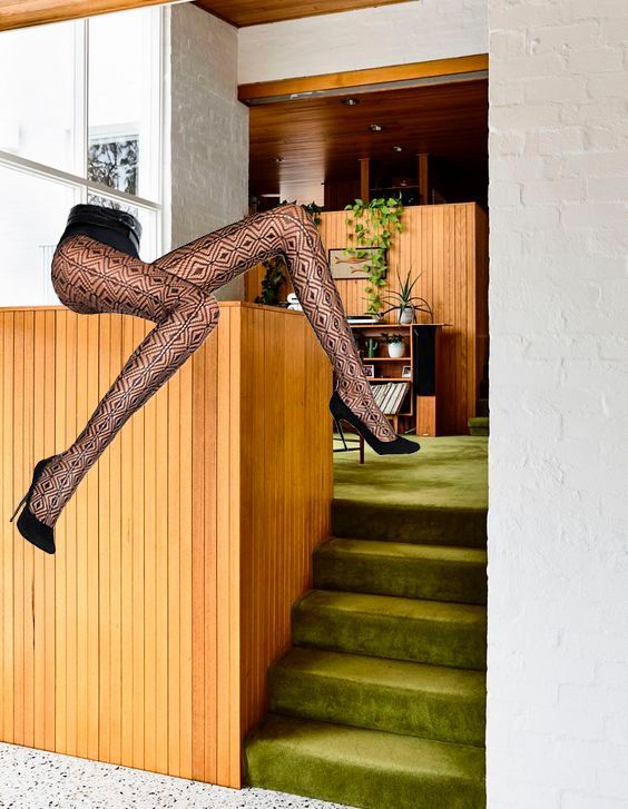 Legs in patterned tights and heels draped over a wooden ledge in a mid-century modern interior.