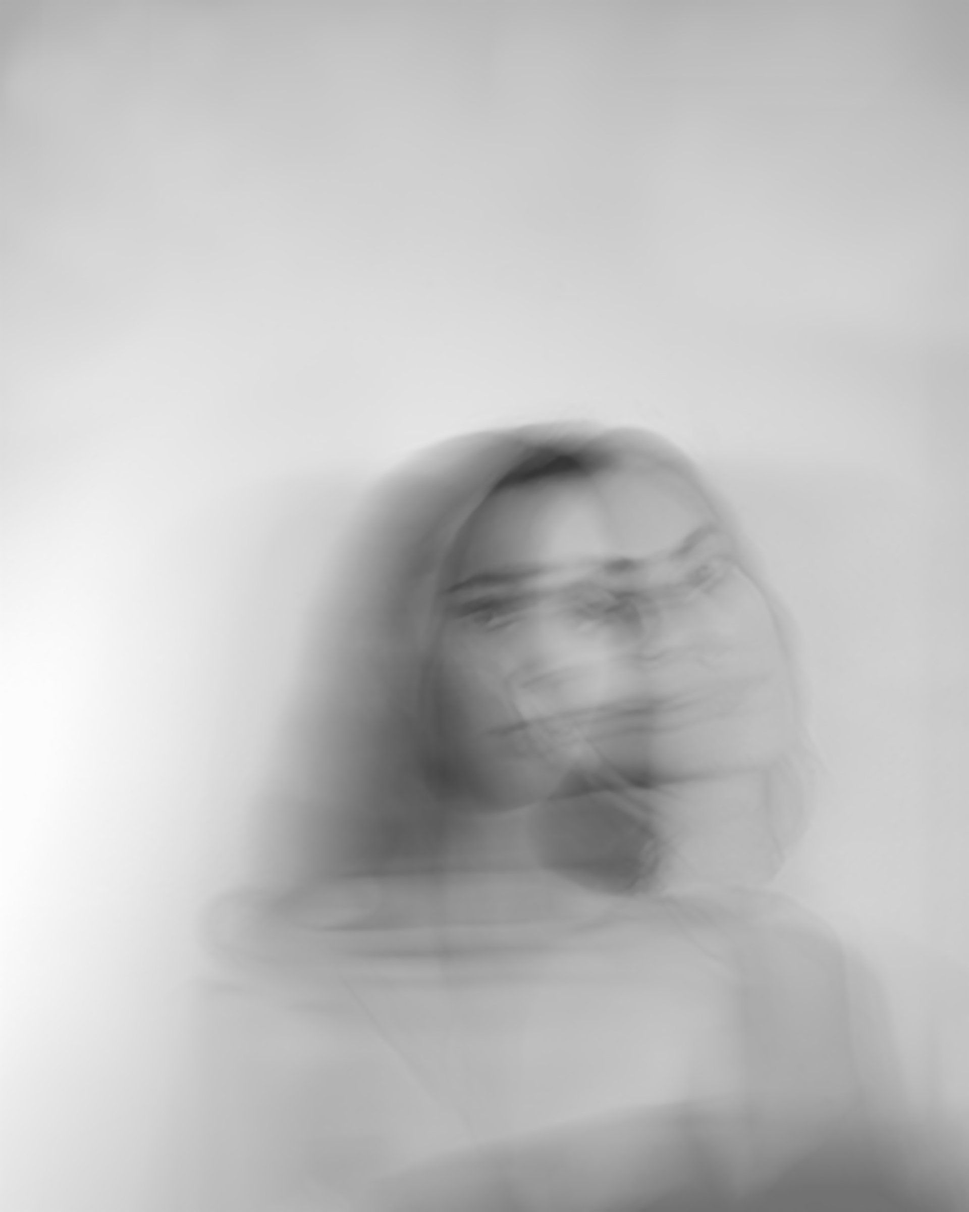 Blurred grayscale photo of a person, face visible, appearing in motion, against a light background.