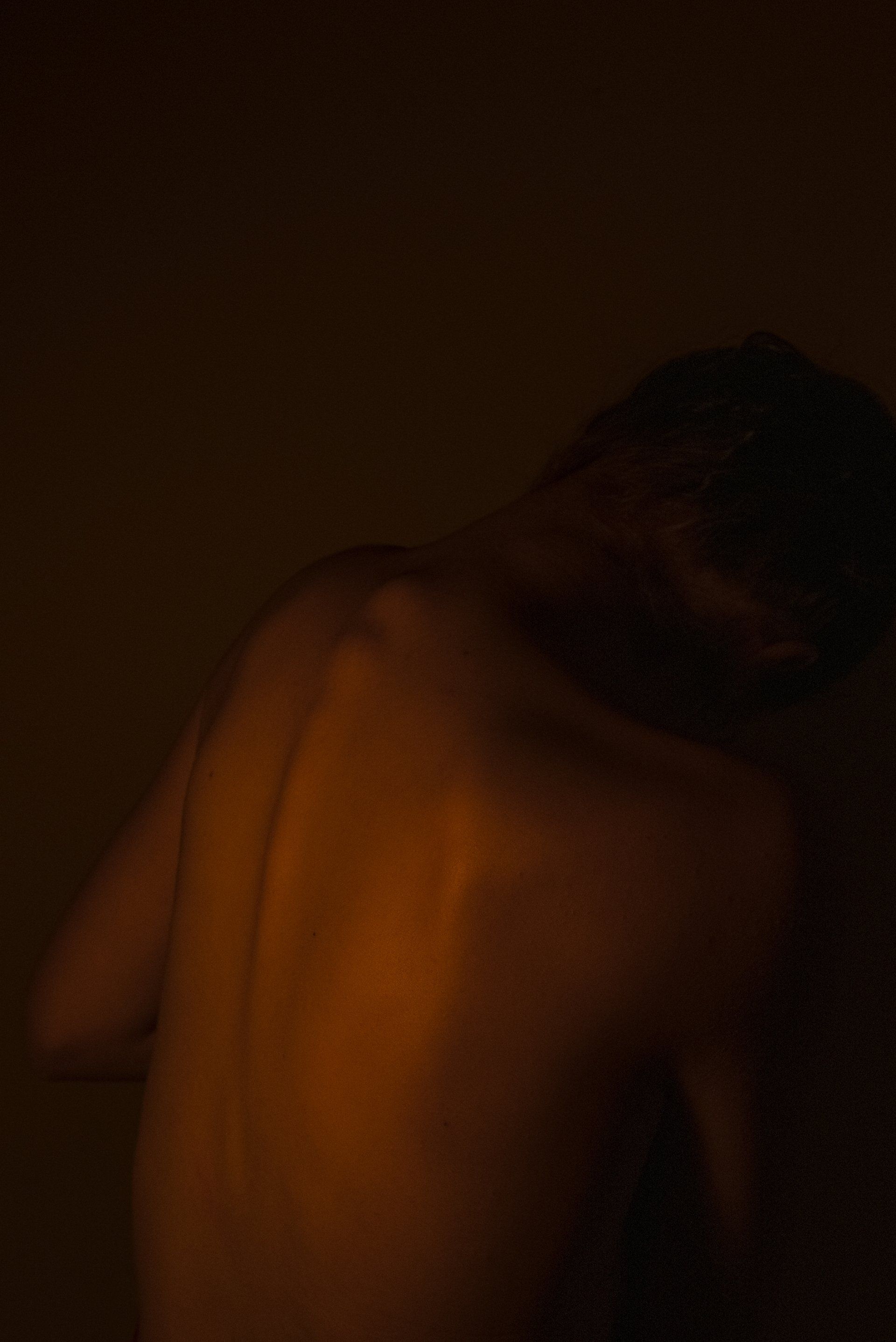 Bare back illuminated by orange light in a dark setting.