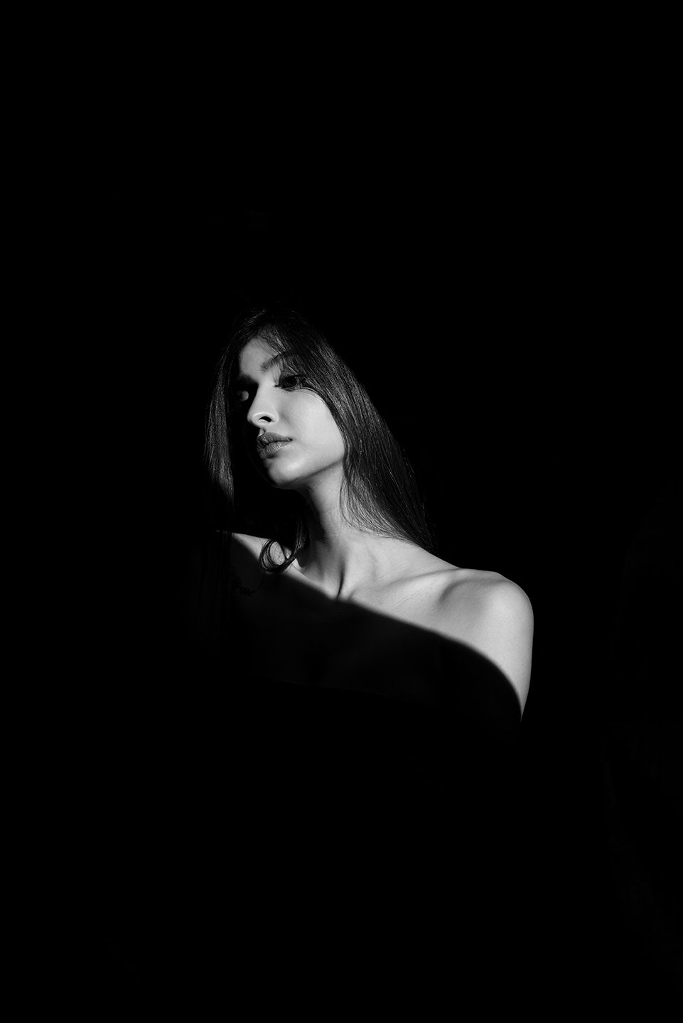 Woman with dark hair, lit by a single light source, in a black and white portrait.