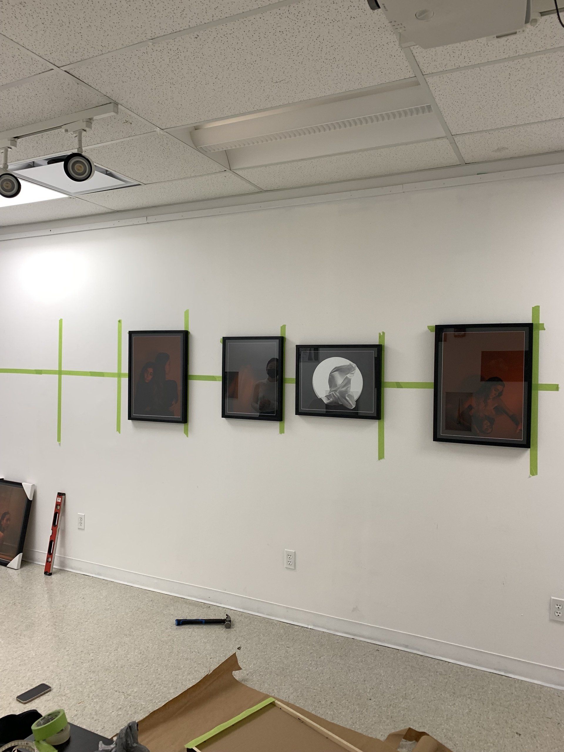 A row of framed pictures taped to a white wall.
