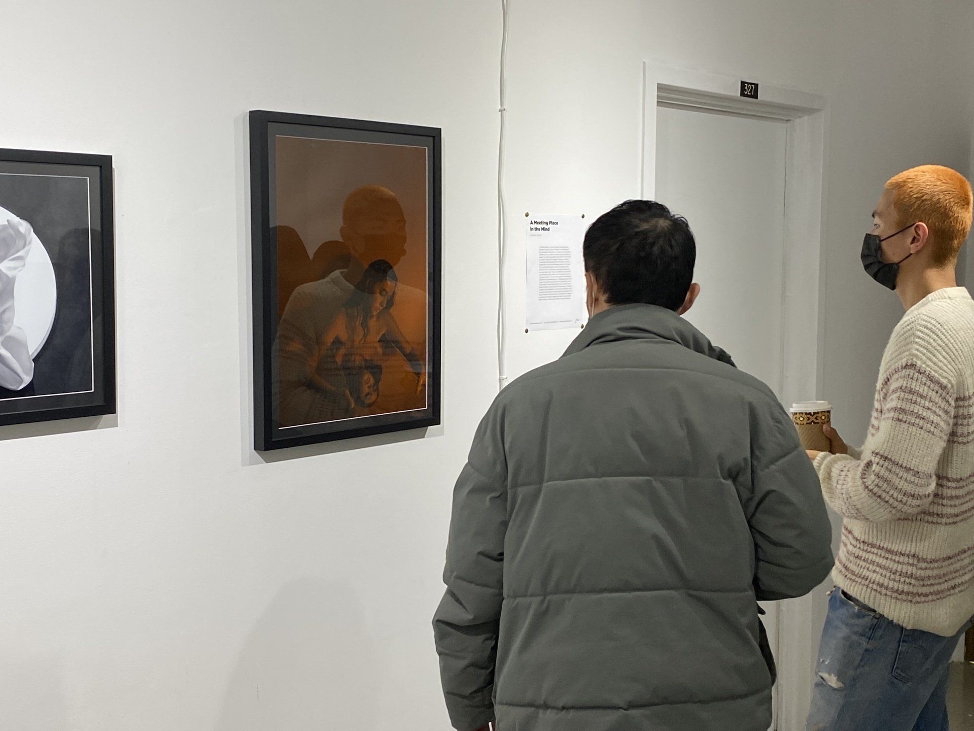 Two men are looking at paintings on a wall.