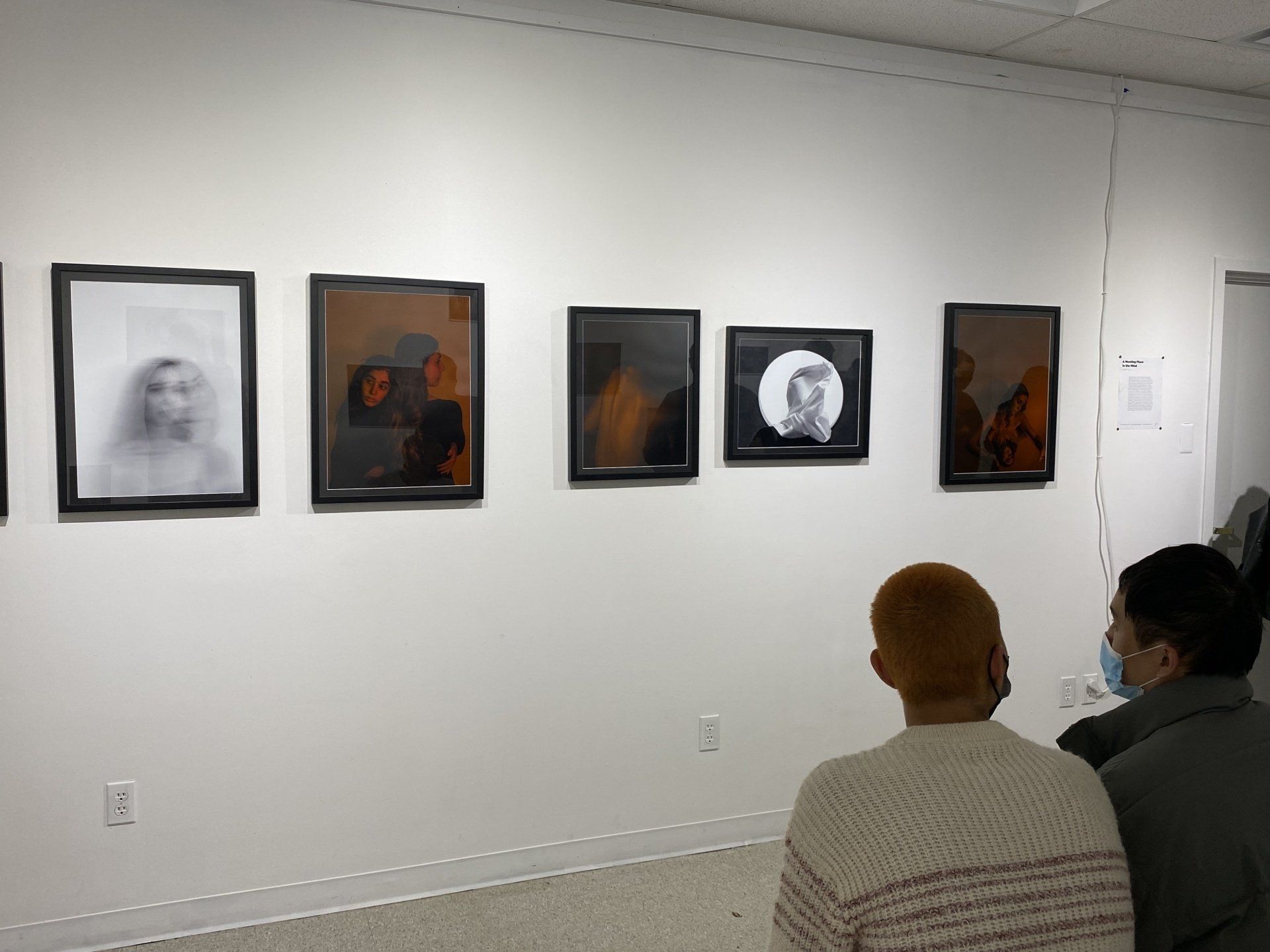 Two people are looking at picutres on a wall.