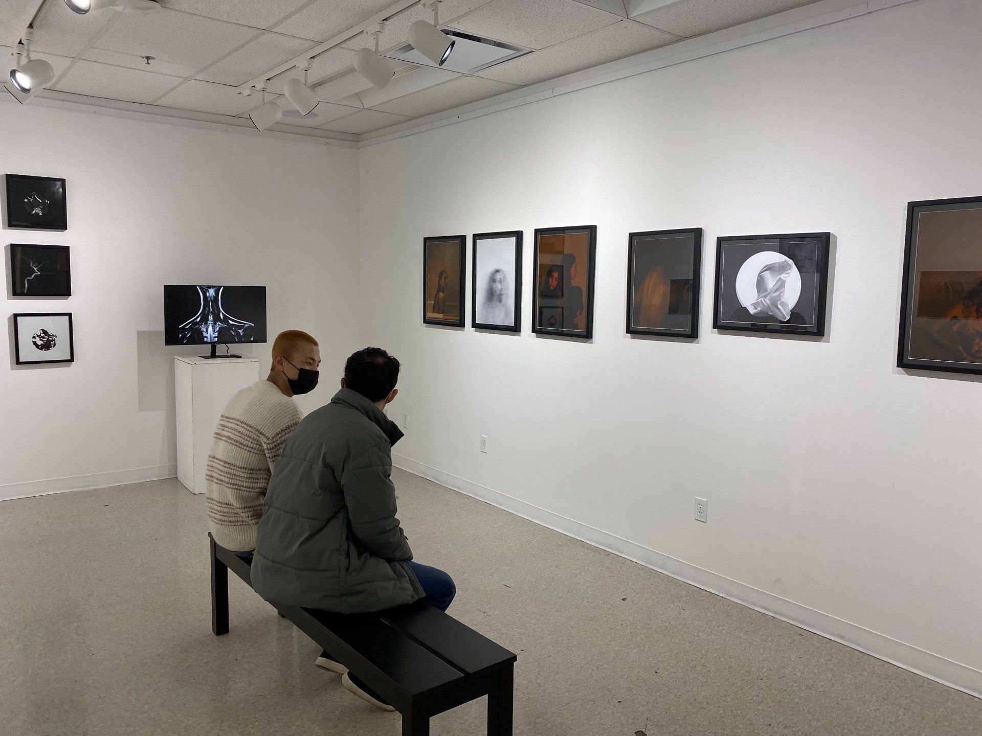 Two people are looking at picutres on a wall.
