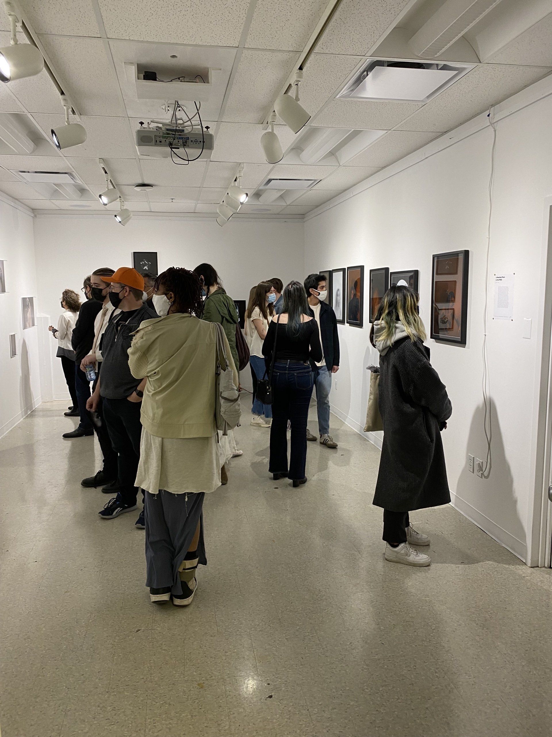 A group of people are looking at pictures on a wall.
