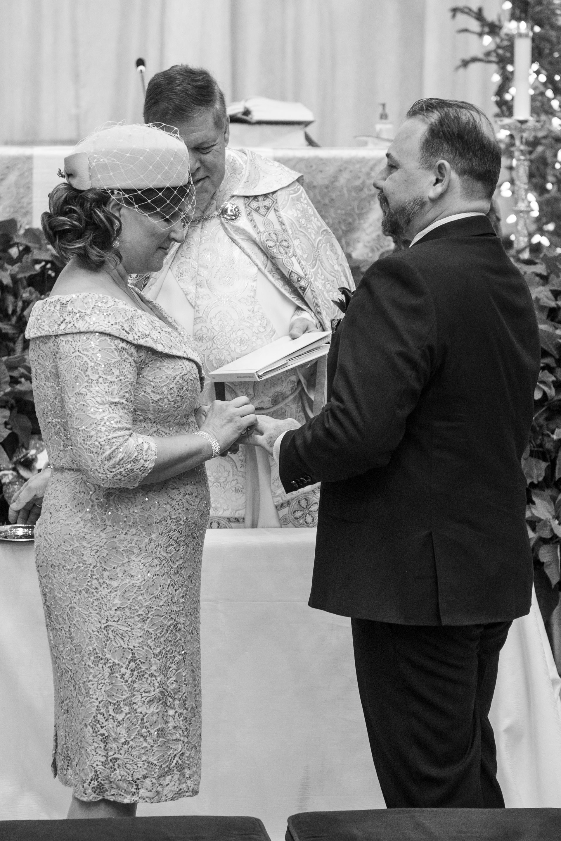 Couple exchanging rings at a wedding ceremony; officiant in background.