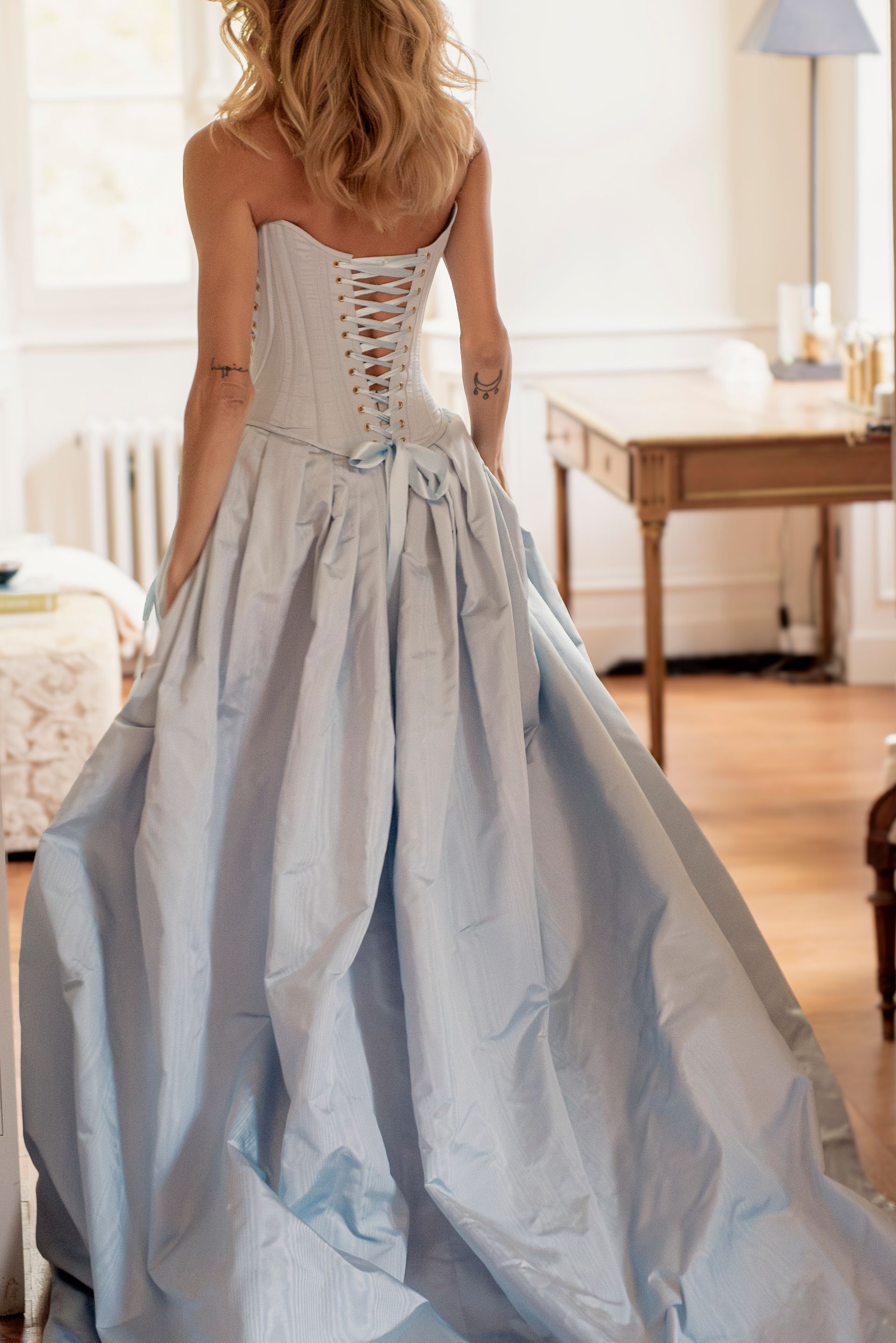 Woman in a light blue strapless gown with a corset back, standing in a room.