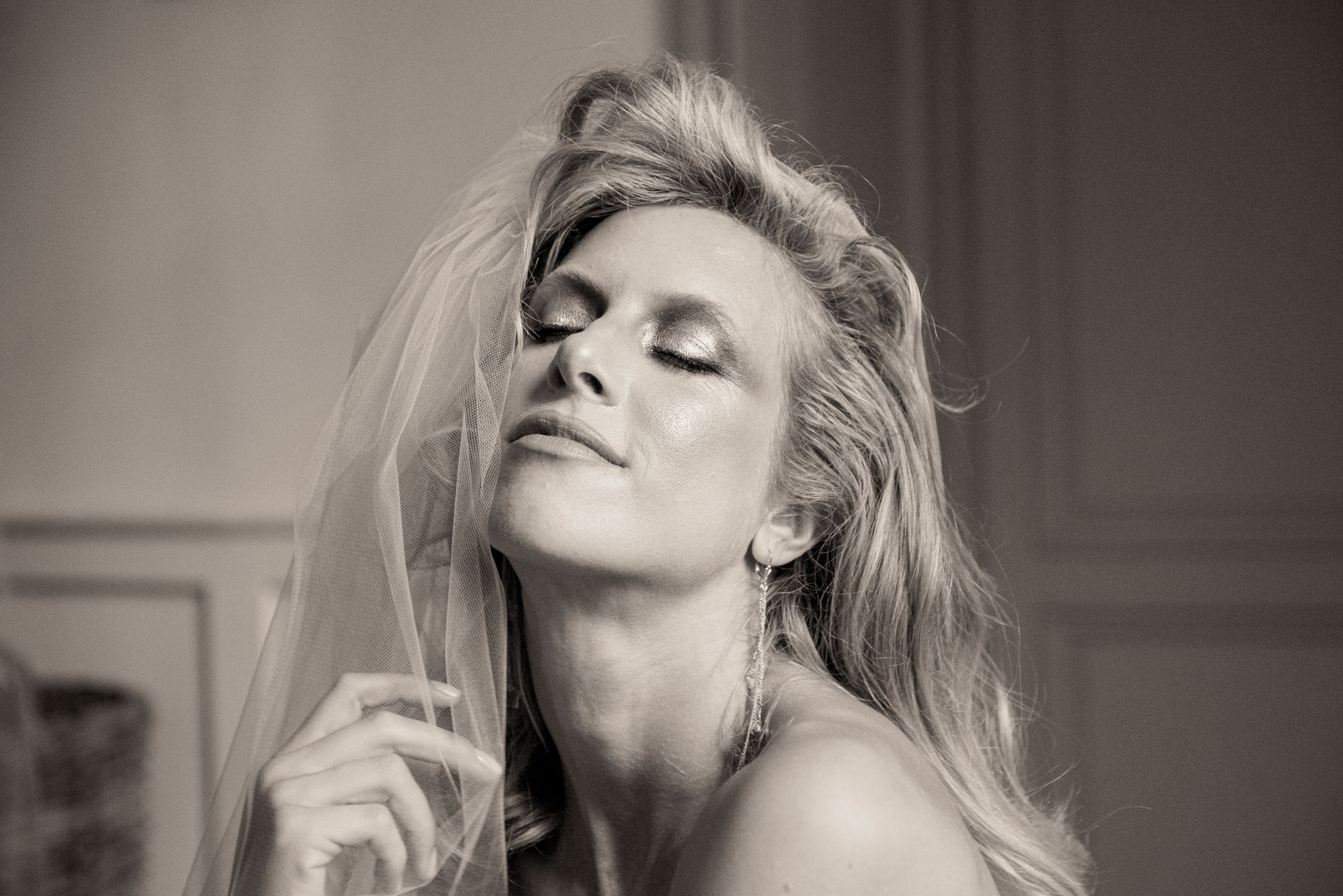 Woman with eyes closed, head tilted back, veil, long blonde hair, sparkling face, soft lighting.