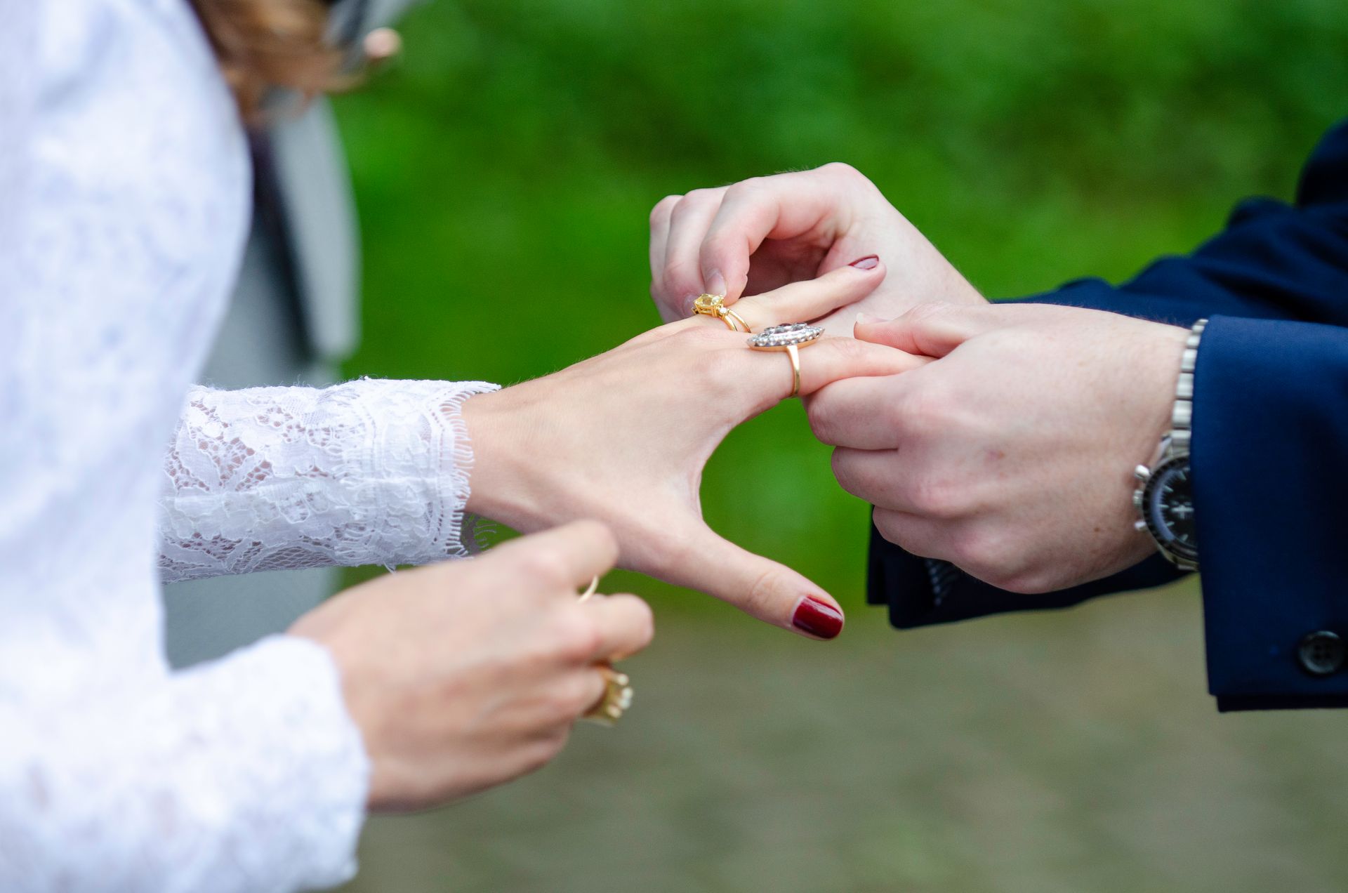 Person places wedding ring on another's finger, outdoors.